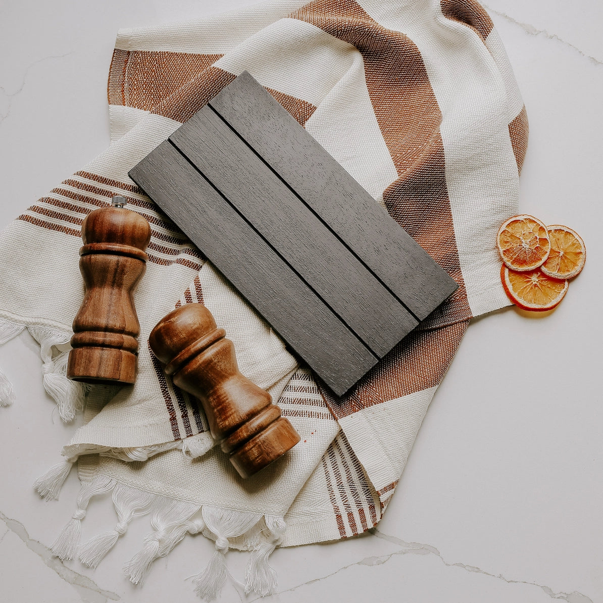 Wooden accent board with wooden salt and pepper shakers on a patterned cloth with dried oranges.