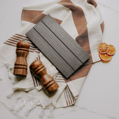 Wooden accent board with wooden salt and pepper shakers on a patterned cloth with dried oranges.