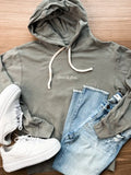 A grey hoodie with white drawstrings and 'Design by James' printed on the chest, styled in a flat lay with light blue jeans and white sneakers on a wooden background.