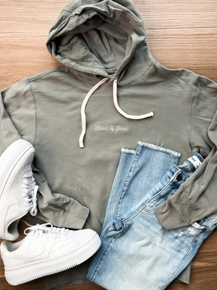 A grey hoodie with white drawstrings and 'Design by James' printed on the chest, styled in a flat lay with light blue jeans and white sneakers on a wooden background.