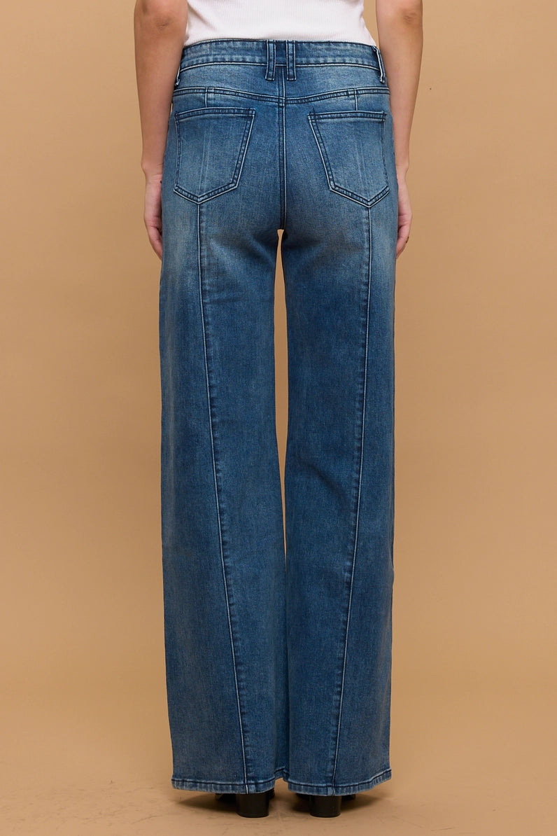 A person shown from the back wearing blue wide-leg denim jeans against a plain tan studio background.