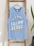 A light blue mineral-wash sleeveless tank top with a white and yellow graphic reading 'BE A REBEL FOLLOW JESUS' hanging on a wooden ladder against a neutral wall.