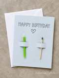 Handmade Happy Birthday greeting card featuring a green candle and matchstick on a light gray textured card with a white envelope.