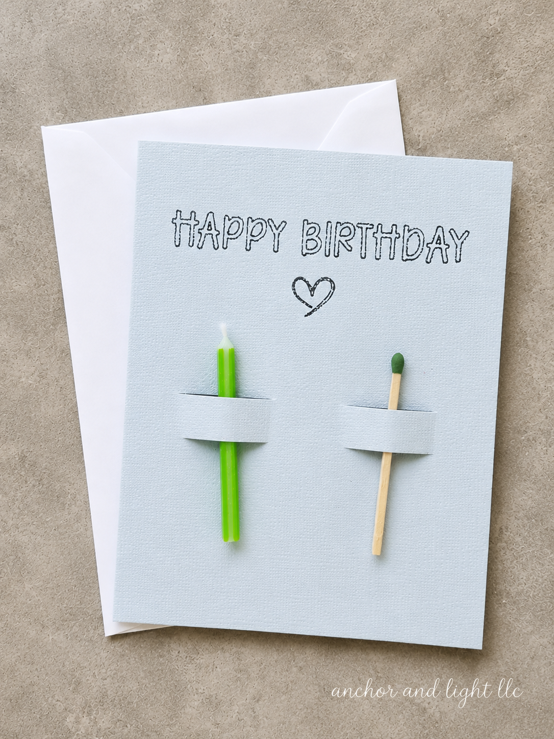 Handmade Happy Birthday greeting card featuring a green candle and matchstick on a light gray textured card with a white envelope.
