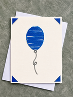 A square cream greeting card featuring a blue balloon illustration with blue corner accents, shown with white envelopes on a textured gray surface.