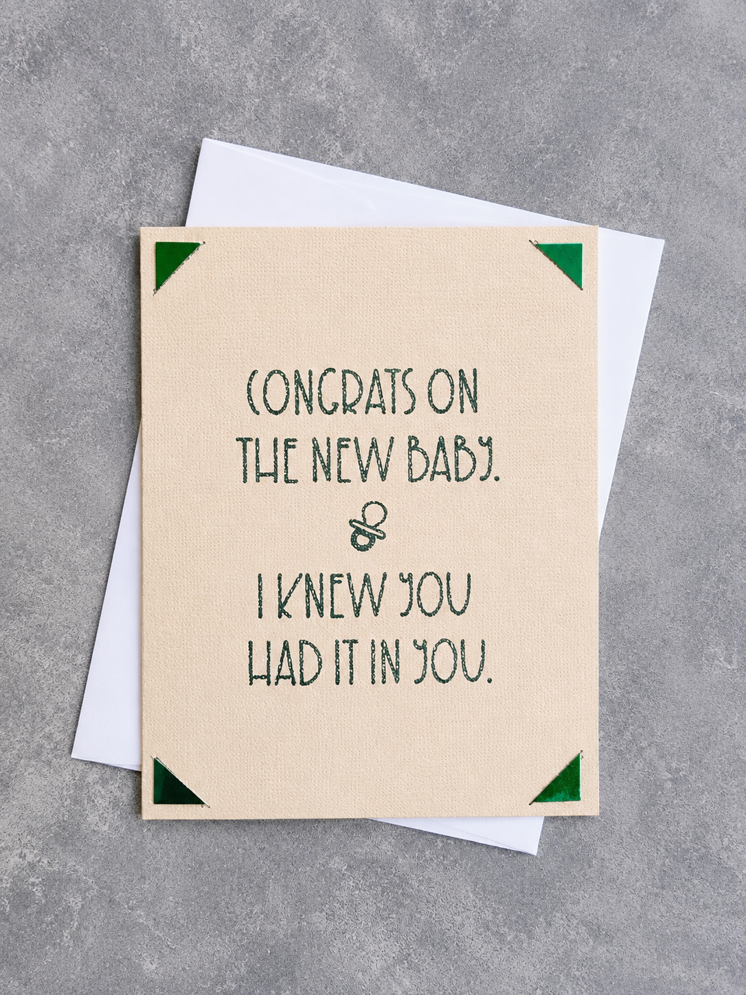 A beige congratulations card with dark green text reading 'CONGRATS ON THE NEW BABY. I KNEW YOU HAD IT IN YOU.