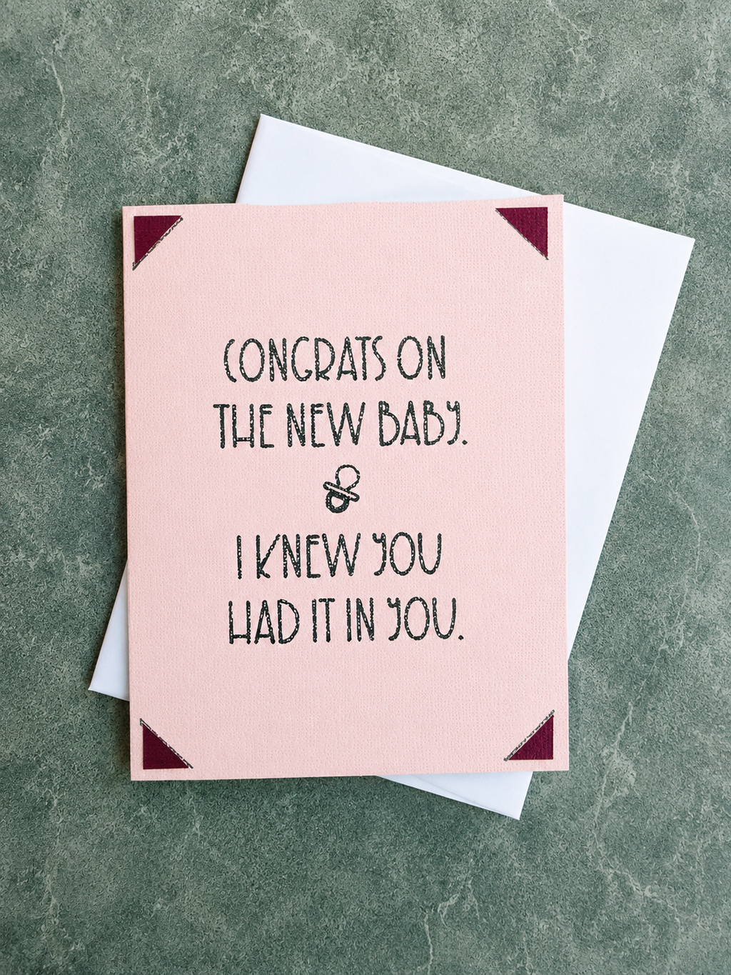 A pink greeting card with black text reading 'CONGRATS ON THE NEW BABY. & I KNEW YOU HAD IT IN YOU.