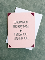A pink greeting card with black text reading 'CONGRATS ON THE NEW BABY. & I KNEW YOU HAD IT IN YOU.