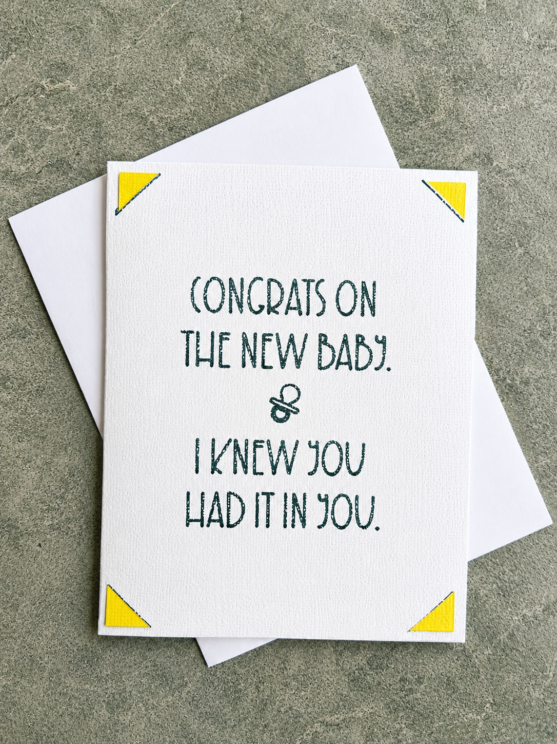 A white greeting card with dark green text reading 'CONGRATS ON THE NEW BABY. & I KNEW YOU HAD IT IN YOU.