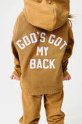 A child wearing a matching tan hoodie and sweatpants set, shown from the back. The hoodie features the phrase 'GOD'S GOT MY BACK' printed in large white arched letters across the upper back.