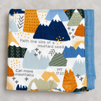 A folded baby blanket with a colorful geometric mountain pattern and Bible verse text, displayed on a neutral gray background.