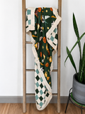 A dark green blanket with a basketball-themed pattern and cream-colored borders, draped over a wooden ladder next to a potted snake plant.