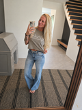 A woman takes a mirror selfie in a home entryway, wearing a light brown cropped t-shirt with a white geometric graphic and light-wash blue flare jeans.