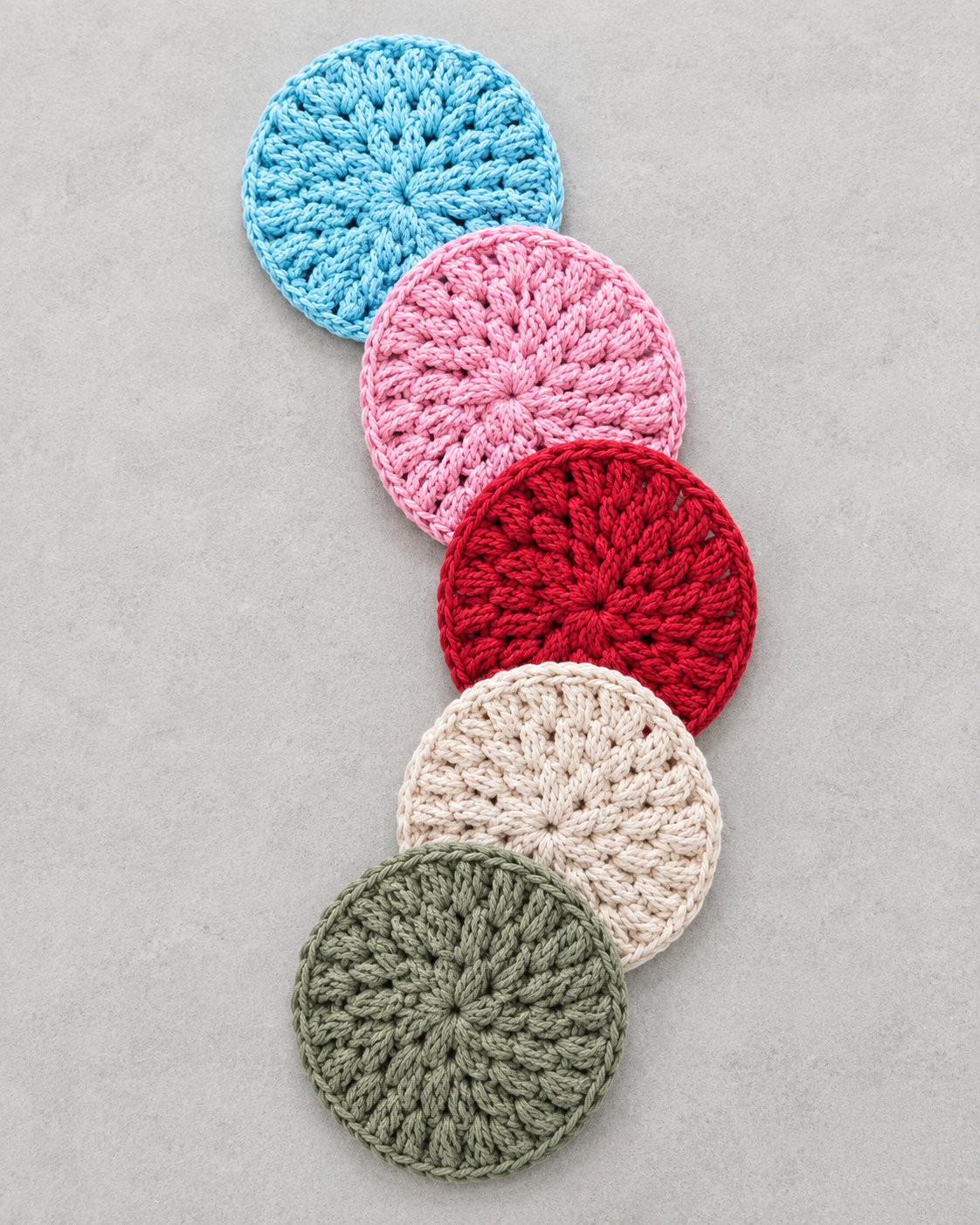 Five round crocheted fabric pieces in light blue, pink, red, cream, and sage green, arranged diagonally on a light gray background.