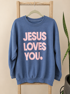 A blue crewneck sweatshirt hanging on a wooden hanger from a wooden ladder, featuring the text 'JESUS LOVES YOU.' in light pink.