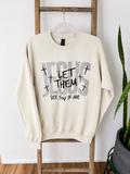 An off-white crewneck sweatshirt hanging on a wooden ladder, featuring a graphic print that reads 'JESUS LET THEM SEE YOU IN ME' with small crosses.