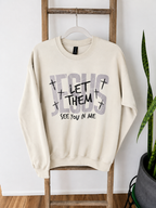 An off-white crewneck sweatshirt hanging on a wooden ladder, featuring a graphic print that reads 'JESUS LET THEM SEE YOU IN ME' with small crosses.