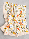 A cotton muslin baby blanket with a colorful floral print and ruffled edges, laid flat on a light gray tiled surface.