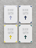 Four square wall art prints arranged in a 2x2 grid on a gray textured background. Each print has the words 'ON YOUR BAPTISM' in black lettering with a cross symbol below, and the corners are decorated with different colored triangle accents in light blue, navy, yellow, and teal.