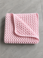 A folded light pink crocheted blanket with a textured openwork pattern, displayed on a gray tiled floor.