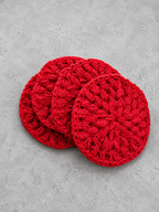 Four round red crocheted coasters stacked slightly offset on a textured gray surface.