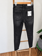 Back view of a pair of dark gray washed skinny jeans hanging on a wooden hanger, displayed on a wooden step stool in an indoor setting.