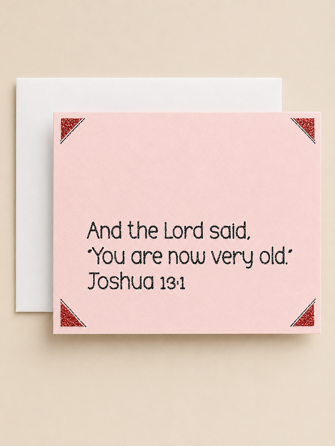 A pink greeting card with a Bible verse printed in black text, shown with a white envelope behind it on a warm beige background.